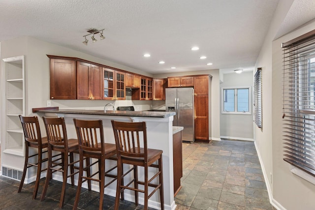 724 Pierce St NE, Minneapolis, MN 55413 - kitchen with stainless steel fridge, stone tile floors, recessed lighting, glass insert cabinets, and a peninsula