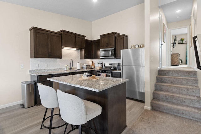 8468 Gateway Cir, Monticello, MN 55362 - kitchen with appliances with stainless steel finishes, dark brown cabinetry, a kitchen bar, light stone counters, and light wood-style floors