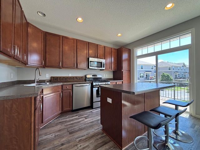 8389 Norwood Ln N, Maple Grove, MN 55369 - kitchen with appliances with stainless steel finishes, dark countertops, dark wood-style floors, a breakfast bar area, and a center island