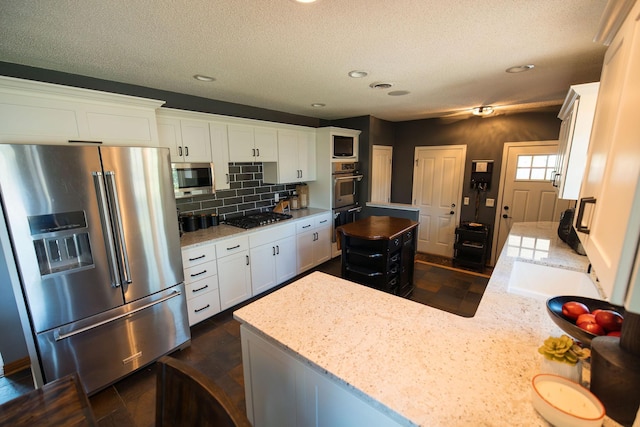 701 Oak Ave, Olivia, MN 56277 - kitchen with stainless steel appliances, decorative backsplash, light stone countertops, white cabinetry, and a textured ceiling