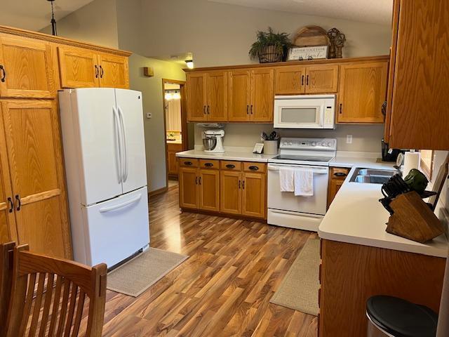 302 Peifer Dr, Litchfield, MN 55355 - kitchen with white appliances, vaulted ceiling, wood finished floors, light countertops, and brown cabinets
