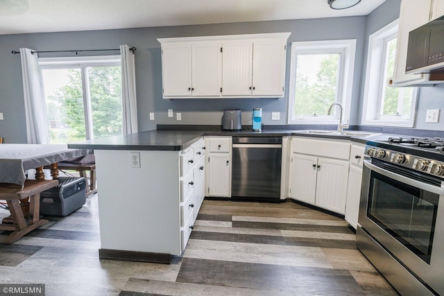 6354 151st Street Ct N, Hugo, MN 55038 - kitchen featuring appliances with stainless steel finishes, a peninsula, wood finished floors, white cabinetry, and dark countertops