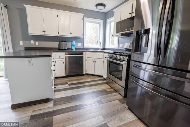 6354 151st Street Ct N, Hugo, MN 55038 - kitchen featuring appliances with stainless steel finishes, a peninsula, dark countertops, light wood-type flooring, and white cabinetry