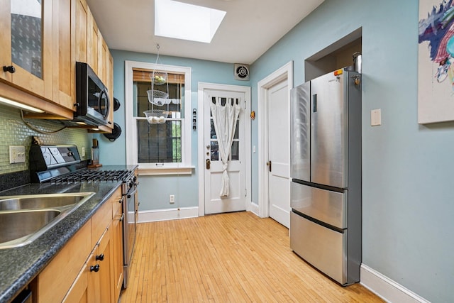1718 Clinton Ave Unit 6, Minneapolis, MN 55404 - kitchen with appliances with stainless steel finishes, a skylight, decorative backsplash, light wood finished floors, and dark stone countertops