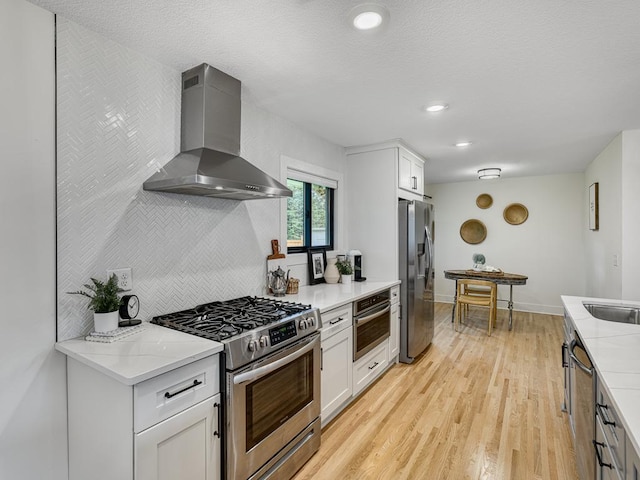 4909 Trillium Ln, Edina, MN 55435 - kitchen featuring wall chimney exhaust hood, stainless steel appliances, light wood-style floors, white cabinets, and light stone counters