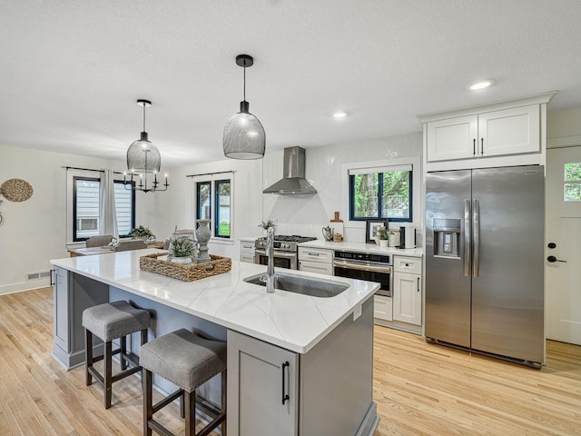 4909 Trillium Ln, Edina, MN 55435 - kitchen featuring appliances with stainless steel finishes, wall chimney range hood, light stone counters, light wood-style flooring, and a kitchen island with sink