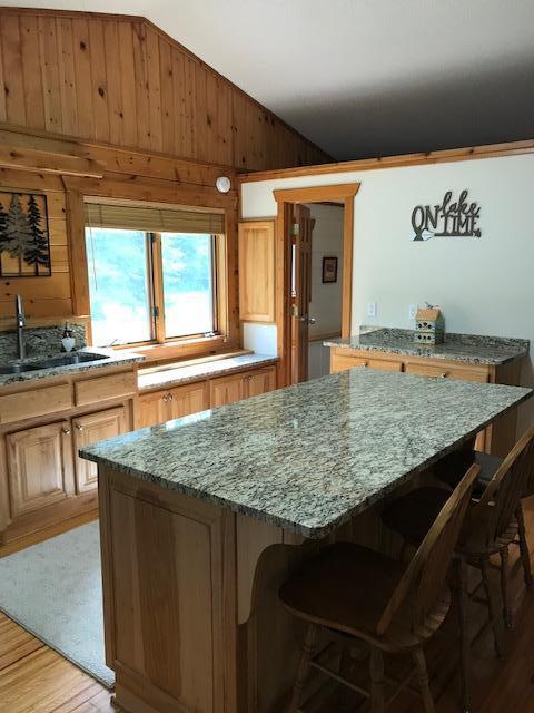 8916 Kabekona Springs Dr NW, Walker, MN 56484 - kitchen featuring lofted ceiling, a center island, wooden walls, light wood-style flooring, and light stone counters