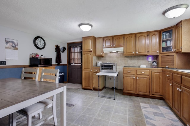 1388 13 1/2 Ave, Barron, WI 54812 - kitchen with stainless steel microwave, brown cabinets, under cabinet range hood, a textured ceiling, and backsplash