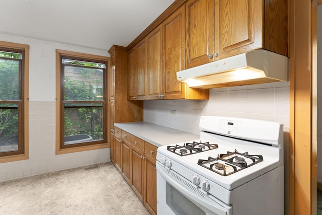 693 Bedford St, Saint Paul, MN 55130 - kitchen featuring white gas range, under cabinet range hood, brown cabinetry, light countertops, and tile walls
