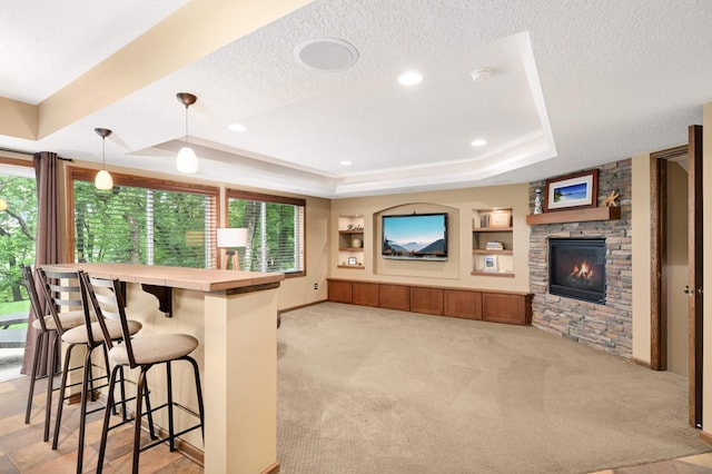 10787 Alison Way, Inver Grove Heights, MN 55077 - kitchen featuring a tray ceiling, a kitchen bar, light carpet, a stone fireplace, and a textured ceiling