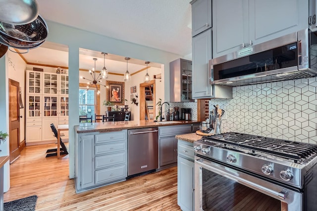 2707 Brighton Ave NE, Minneapolis, MN 55418 - kitchen with stainless steel appliances, light wood finished floors, a peninsula, a chandelier, and decorative backsplash