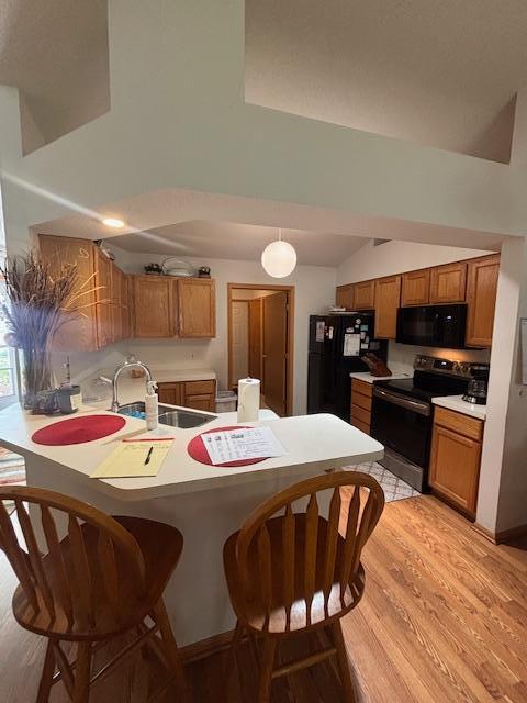 9257 Prairieview Trl N, Champlin, MN 55316 - kitchen with black appliances, a peninsula, brown cabinetry, vaulted ceiling, and a kitchen breakfast bar