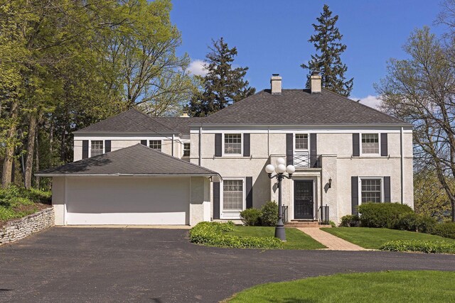 17950 Breezy Point Rd, Woodland, MN 55391 - colonial house featuring a chimney, driveway, stucco siding, an attached garage, and a front lawn