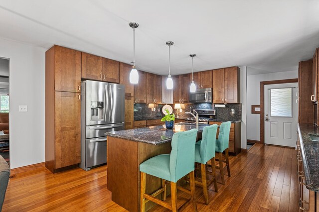 8544 Demontreville Trl N, Lake Elmo, MN 55042 - kitchen with stainless steel appliances, dark wood-style floors, backsplash, dark stone countertops, and a center island with sink