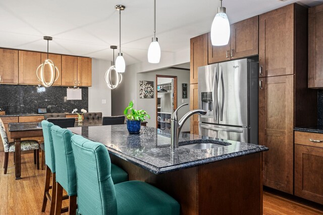 8544 Demontreville Trl N, Lake Elmo, MN 55042 - kitchen with stainless steel fridge, light wood-type flooring, decorative backsplash, a breakfast bar, and dark stone countertops