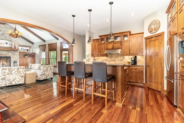 19270 Foxfield Dr, Credit River Twp, MN 55372 - kitchen with under cabinet range hood, brown cabinets, arched walkways, dark wood-type flooring, and backsplash