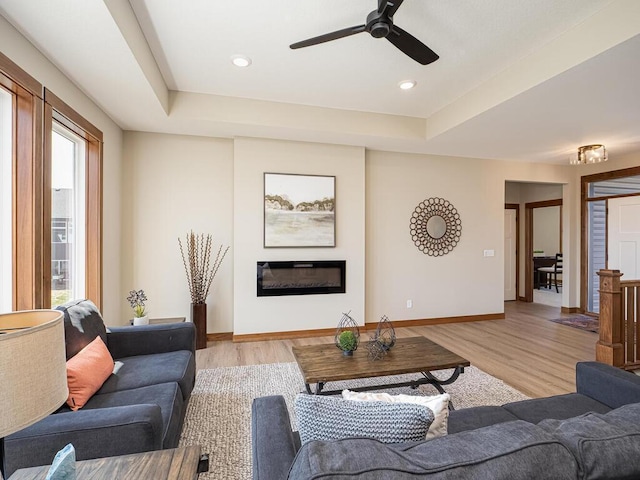 1136 168th Ln NW, Andover, MN 55304 - living room with light wood finished floors, a glass covered fireplace, a tray ceiling, and ceiling fan