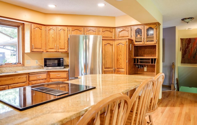 13445 190th Ave NW, Elk River, MN 55330 - kitchen with freestanding refrigerator, light stone counters, stovetop with downdraft, a kitchen breakfast bar, and light wood-style floors