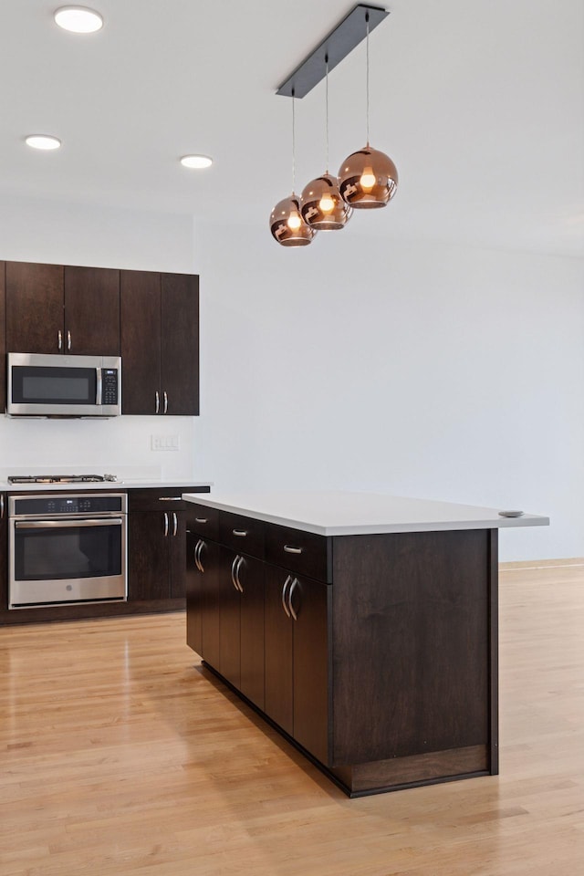 1240 2nd St Unit 1024, Minneapolis, MN 55415 - kitchen featuring appliances with stainless steel finishes, light wood-type flooring, light countertops, decorative light fixtures, and dark brown cabinets