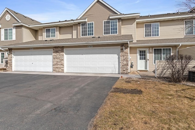 10787 Unity Ln N, Brooklyn Park, MN 55443 - view of property featuring stone siding, driveway, an attached garage, and roof with shingles