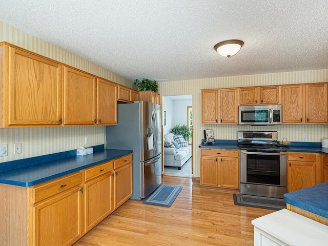 18232 Roosevelt St NW, Elk River, MN 55330 - kitchen featuring appliances with stainless steel finishes, wallpapered walls, a textured ceiling, light wood-style floors, and dark countertops