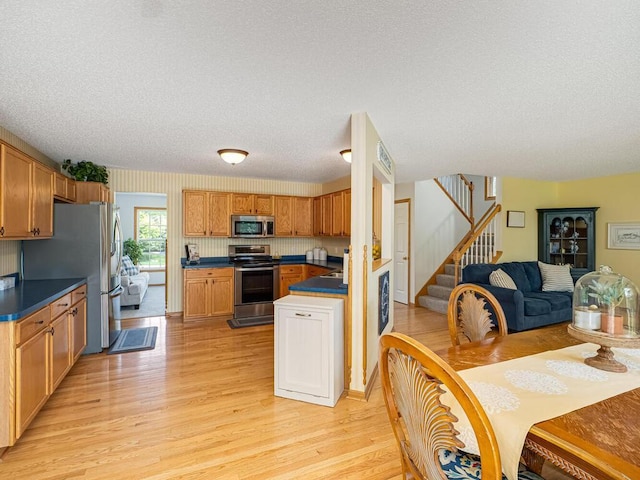 18232 Roosevelt St NW, Elk River, MN 55330 - kitchen featuring appliances with stainless steel finishes, light wood finished floors, open floor plan, dark countertops, and a textured ceiling