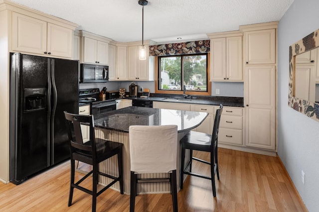 2900 16th Ave S, Moorhead, MN 56560 - kitchen with black appliances, cream cabinets, light wood-type flooring, a breakfast bar area, and hanging light fixtures