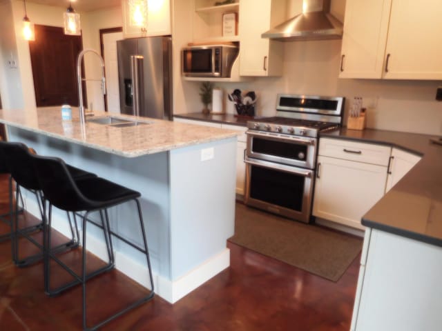 14650 Hilltop Rd, Ashby, MN 56309 - kitchen featuring stainless steel appliances, wall chimney range hood, white cabinetry, decorative light fixtures, and a kitchen island with sink
