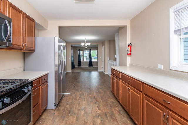 634 11th St N, Moorhead, MN 56560 - kitchen with stainless steel microwave, black gas range oven, a chandelier, dark wood-type flooring, and brown cabinetry