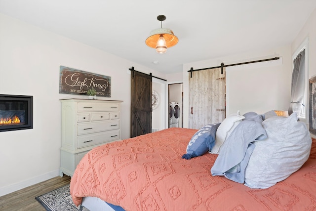 26887 709th St, Lake City, MN 55041 - bedroom featuring a barn door, washer and dryer, wood finished floors, and a glass covered fireplace