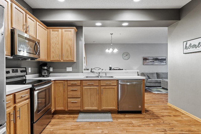 11122 Aberdeen St NE Unit C, Blaine, MN 55449 - kitchen featuring appliances with stainless steel finishes, a peninsula, light wood finished floors, light countertops, and hanging light fixtures