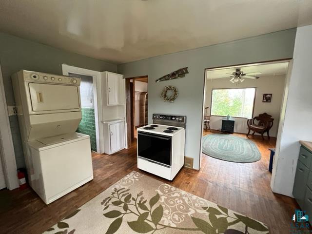 355 Harvey St, Ely, MN 55731 - kitchen featuring electric stove, estacked washer and dryer, wood finished floors, white cabinetry, and ceiling fan