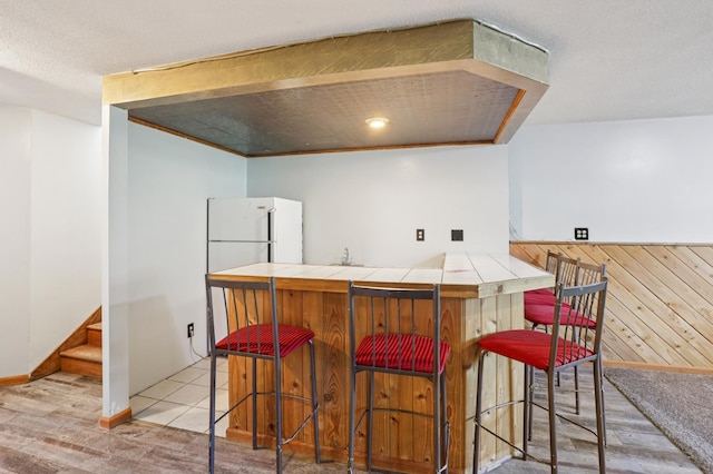 733 Meadow Dr, Hudson, WI 54016 - kitchen featuring tile countertops, light wood-style floors, wood walls, a breakfast bar area, and a peninsula