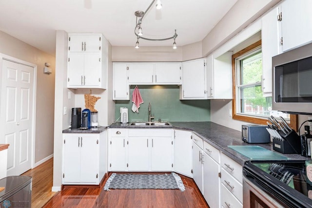 1124 15th St N, Moorhead, MN 56560 - kitchen with appliances with stainless steel finishes, dark countertops, dark wood-type flooring, white cabinetry, and backsplash