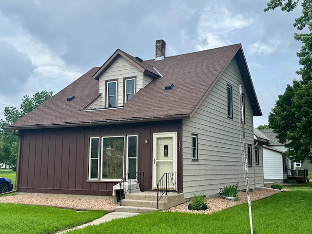 720 Fir Ave, Bird Island, MN 55310 - view of front facade featuring a chimney, board and batten siding, a front yard, and roof with shingles