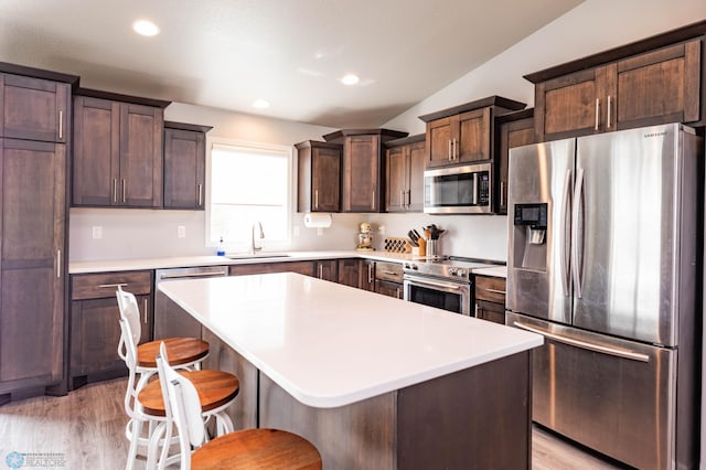 4701 11th St W, West Fargo, ND 58078 - kitchen featuring appliances with stainless steel finishes, dark brown cabinets, a kitchen island, light wood finished floors, and a breakfast bar
