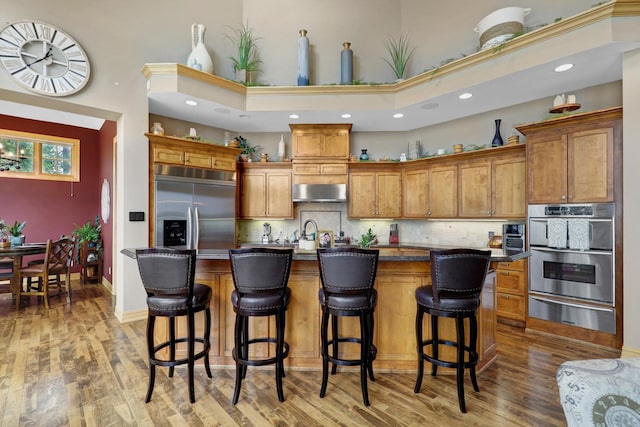 22620 Hayward Ave N, Forest Lake, MN 55025 - kitchen featuring stainless steel appliances, a high ceiling, a warming drawer, brown cabinetry, and wood finished floors