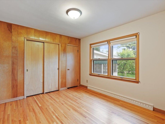 517 Cedar St, Brainerd, MN 56401 - unfurnished bedroom with multiple closets, a baseboard heating unit, light wood-style flooring, and wooden walls