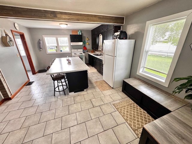420 7th St, Marshall, MN 56258 - kitchen featuring white appliances, dark cabinetry, light countertops, a breakfast bar, and a kitchen island