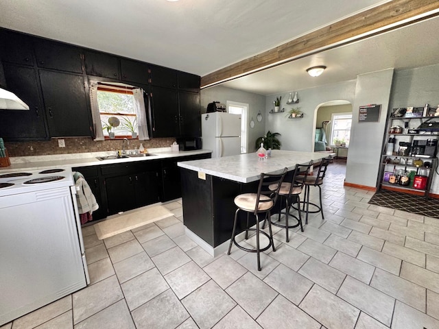 420 7th St, Marshall, MN 56258 - kitchen with dark cabinets, white appliances, arched walkways, light countertops, and beam ceiling