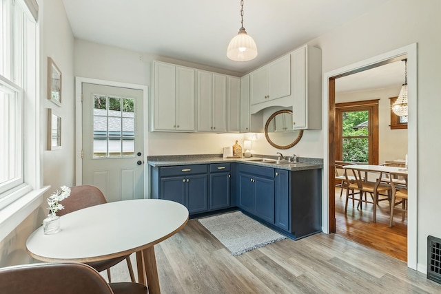 1112 29th Ave NE, Minneapolis, MN 55418 - kitchen featuring blue cabinets, light wood finished floors, hanging light fixtures, and white cabinetry