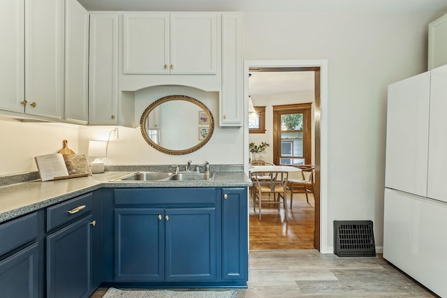 1112 29th Ave NE, Minneapolis, MN 55418 - kitchen featuring blue cabinetry, freestanding refrigerator, light wood finished floors, and white cabinets