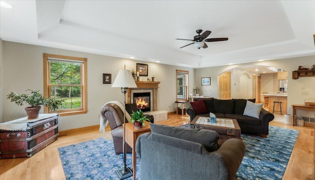 1764 State 84 SW, Pine River, MN 56474 - living room featuring a tray ceiling, arched walkways, a glass covered fireplace, a ceiling fan, and light wood-style flooring