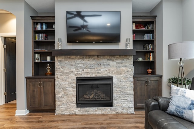 2745 Sand Trap Rd SE, Rochester, MN 55904 - living room featuring wood finished floors, a ceiling fan, a stone fireplace, arched walkways, and built in features