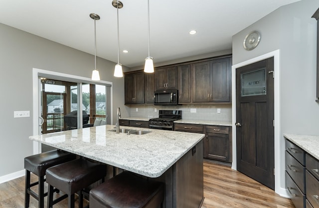 2745 Sand Trap Rd SE, Rochester, MN 55904 - kitchen featuring black appliances, backsplash, dark brown cabinets, wood finished floors, and a center island with sink