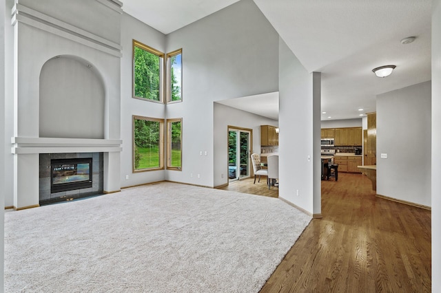 8051 Enclave Bay, Woodbury, MN 55125 - unfurnished living room featuring light wood-style floors, a tile fireplace, and a towering ceiling