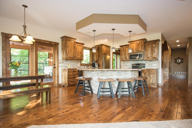 8271 Barton Ave NW, Buffalo, MN 55313 - kitchen with stainless steel appliances, dark wood-type flooring, backsplash, brown cabinetry, and a kitchen island