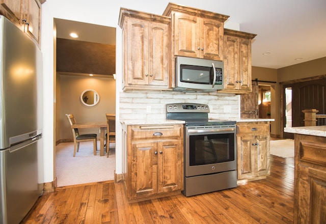 8271 Barton Ave NW, Buffalo, MN 55313 - kitchen featuring stainless steel appliances, backsplash, dark wood-style floors, a barn door, and light stone countertops