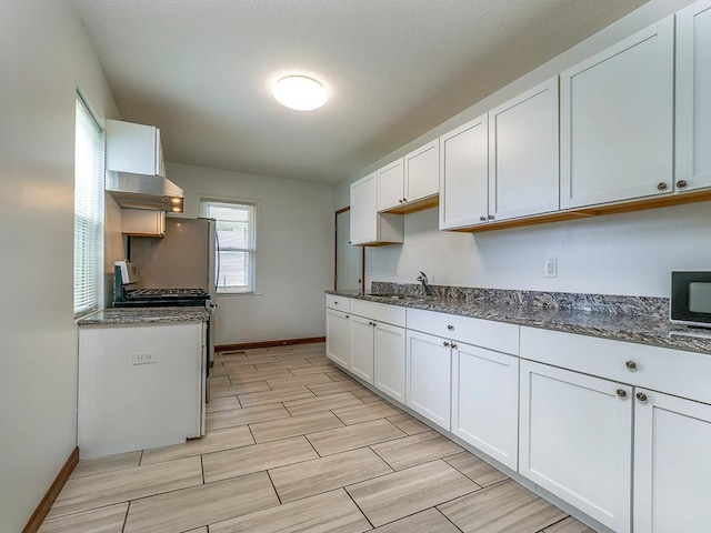 4021 Colfax Ave N, Minneapolis, MN 55412 - kitchen featuring range hood, white cabinetry, wood tiled floors, stainless steel gas stove, and dark stone counters
