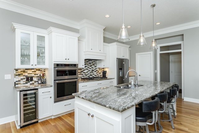 1062 Fox Hill Ln SW, Rochester, MN 55902 - kitchen featuring beverage cooler, appliances with stainless steel finishes, tasteful backsplash, white cabinetry, and a kitchen island with sink